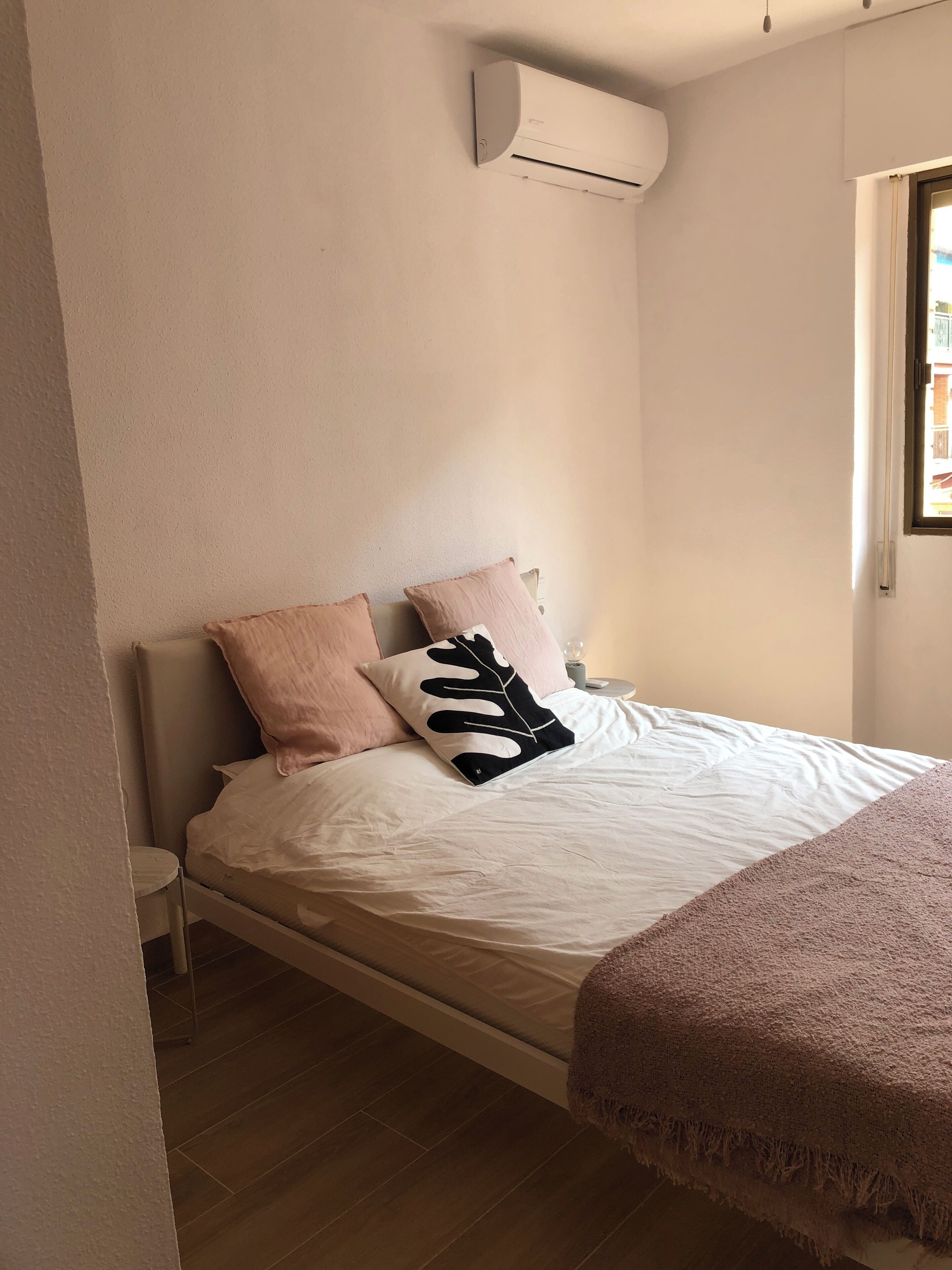 A bedroom with a bed, a nightstand, a bedside table, and an air conditioning unit mounted on the wall.