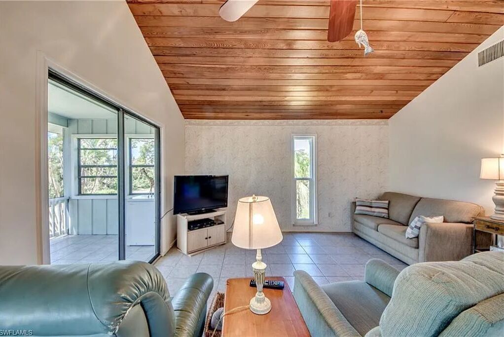 Un soggiorno con soffitto in legno, una televisione, un divano e una lampada.