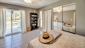 A bedroom with a bed, a large window with curtains, a wardrobe, and a ceiling fan.