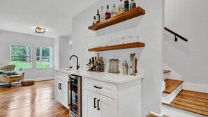A modern kitchen with white cabinetry, wooden shelves holding bottles and glasses, and a built-in oven. - Modern Farmhouse in the City -  4-bedroom house in charming Atlanta (Atlanta)
