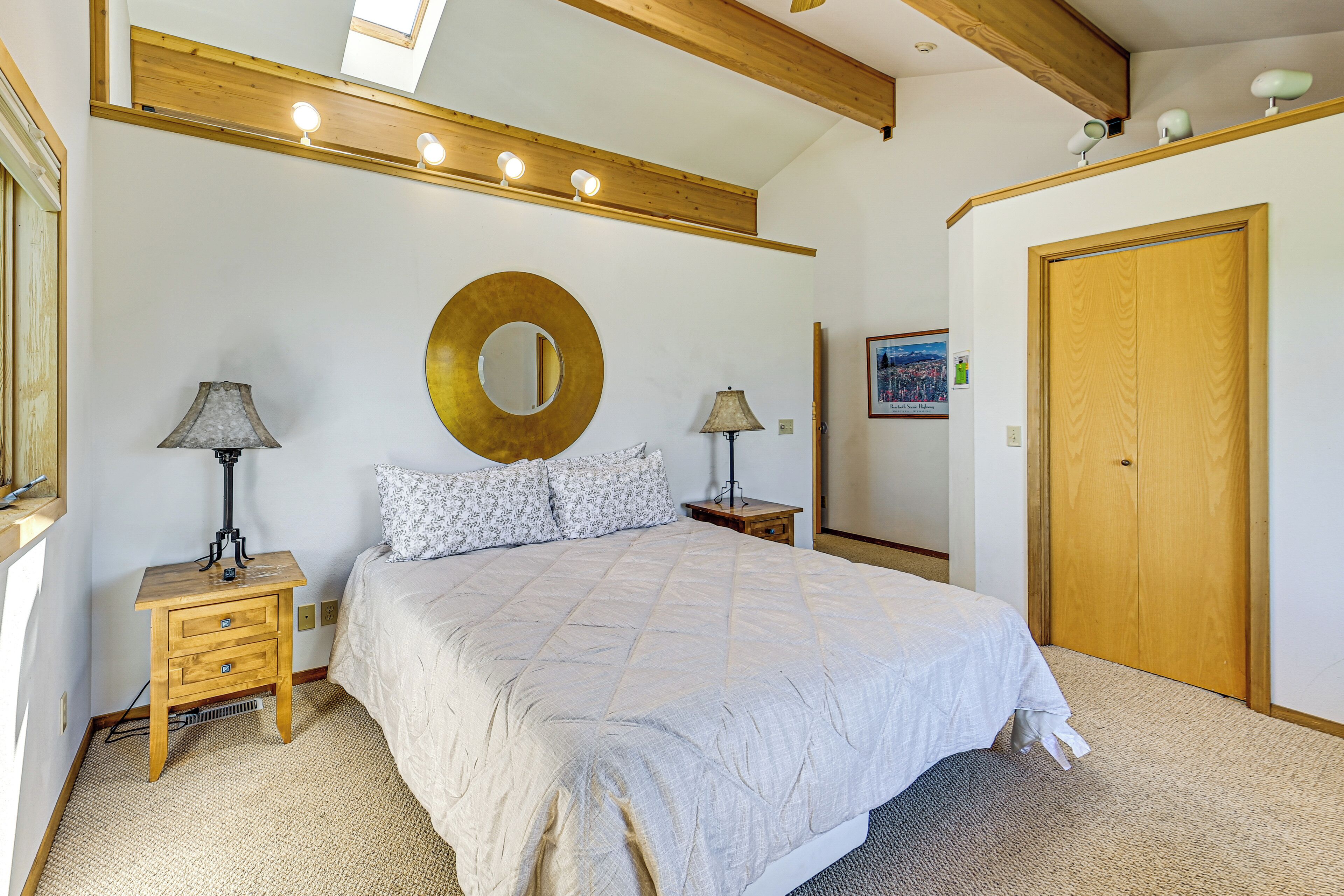 Ein Schlafzimmer mit einem großen Bett, zwei Nachttischen mit Lampen, einer Holzbalkendecke, einem runden Spiegel und einem Kleiderschrank.