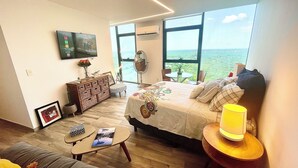 A modern bedroom with a large bed, a bedside table, a small table with a book, a dresser, and a TV mounted on the wall. - Acogedor estudio en Adamant Cabo Norte en Merida, perfecto parejas o home office (Mérida)