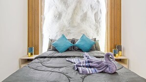 A bed with a striped blanket, two blue pillows, and a purple towel shaped like a swan.
