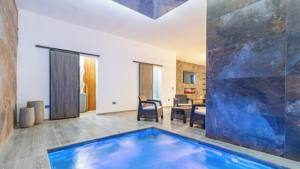A modern indoor pool area with a clear view of the pool, seating area, and a sliding door leading to another room.