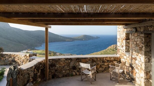 A stone-walled outdoor seating area with a view of the sea and hills.