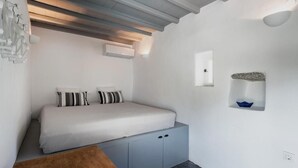 A bedroom with a bed, a wooden table, a grey cabinet, and a small shelf with a bowl.