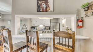 A modern kitchen with white cabinets, a central island, and a dining area with wooden chairs. - 1 Block to Hiking: Ruidoso Home w/ Game Room (Ruidoso)
