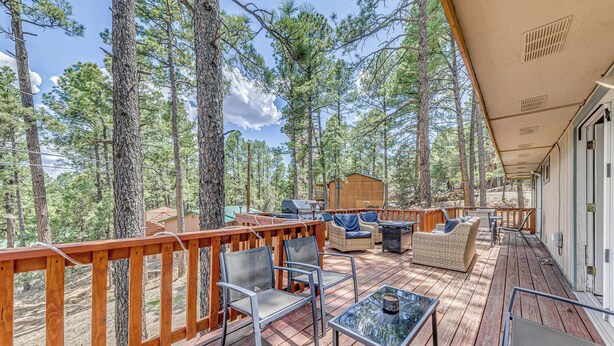 A wooden deck with outdoor furniture, including chairs and a table, overlooking a forest. - 1 Block to Hiking: Ruidoso Home w/ Game Room (Ruidoso)