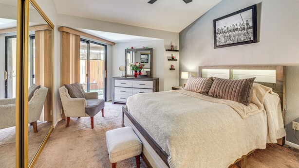 Une chambre  à coucher avec un grand lit, une chaise, une commode et un ventilateur de plafond.
