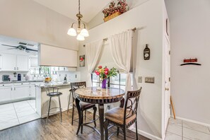 A kitchen with white cabinets, a round dining table with chairs, a ceiling fan, and a window with white curtains. - Mesa Haven w/ Patio, Heated Pool & Hot Tub Access (Mesa)