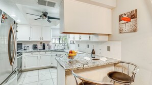 Une cuisine moderne avec des armoires blanches, un comptoir en granit et un ventilateur de plafond.