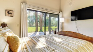 A bedroom with a large bed, a television mounted on the wall, and a window with a view of trees and grass. - Golf Course Getaway & Hot Tub Haven in Pinetop! (Pinetop)