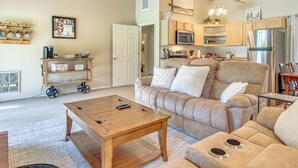 A cozy living room with a wooden coffee table, beige sofa, and a kitchen area with wooden cabinets and appliances. - Golf Course Getaway & Hot Tub Haven in Pinetop! (Pinetop)