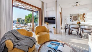 A modern living room with a sofa, armchair, and a dining area with a table and chairs. - Hg06 Adjacent to Aphrodite Hills- Private Pool (Kouklia)