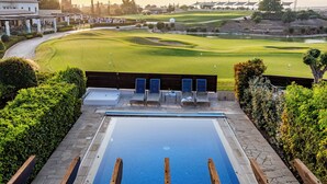 A pool area with lounge chairs, a view of a golf course, and a building in the background. - Hg06 Adjacent to Aphrodite Hills- Private Pool (Kouklia)