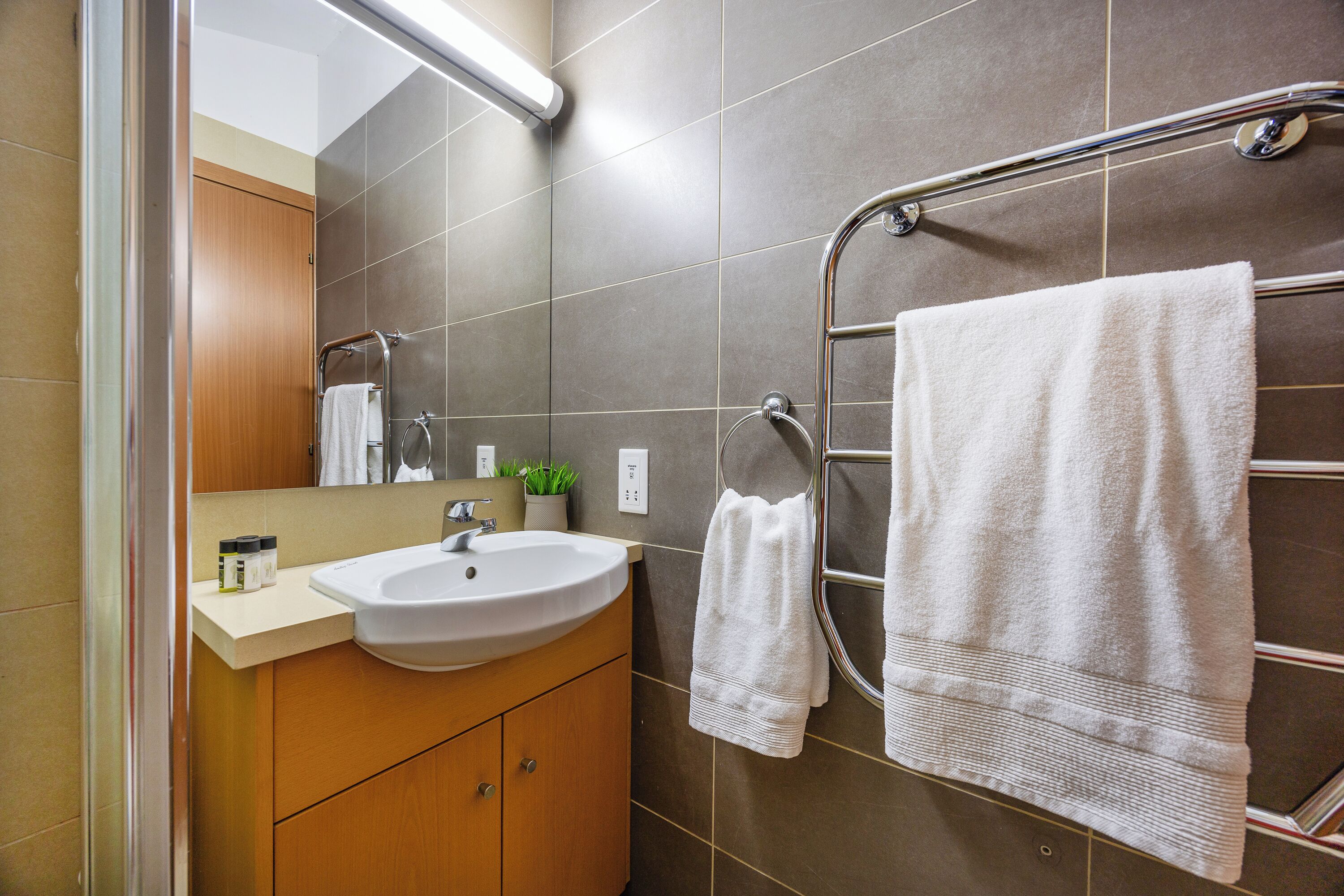 A modern bathroom with a sink, mirror, towel rack, and wooden cabinets.