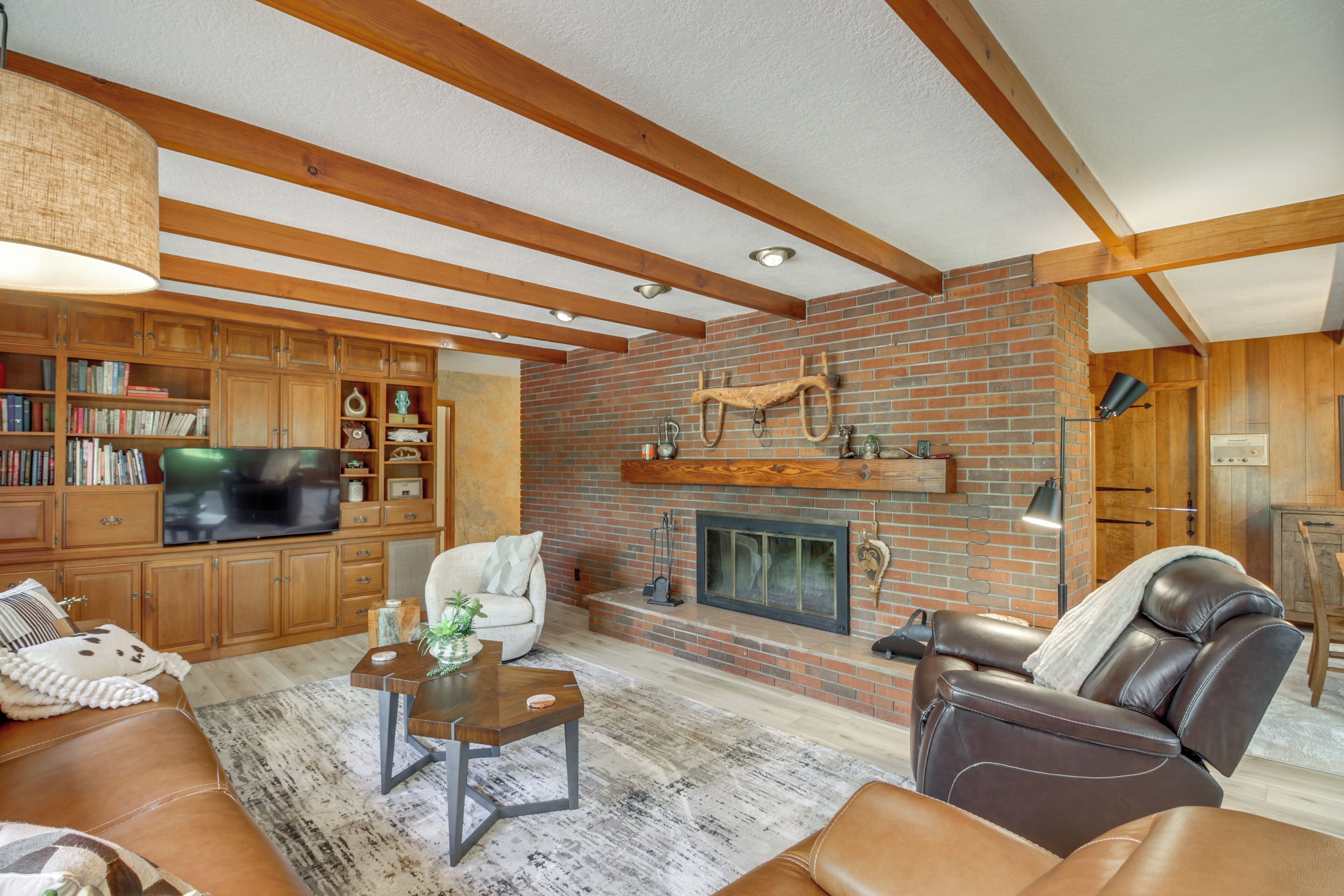 A living room with a fireplace, wooden beams, a television, and a leather sofa.