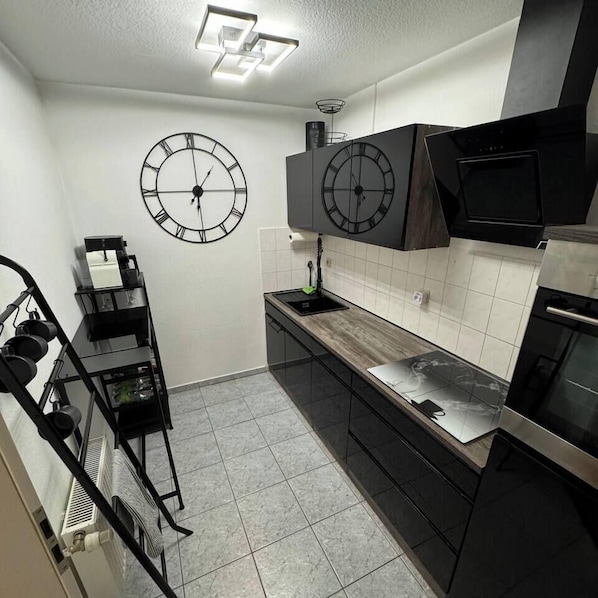 Eine moderne Küche mit zwei Wanduhren, einem Edelstahl-Kühlschrank und einem schwarzen Backofen.