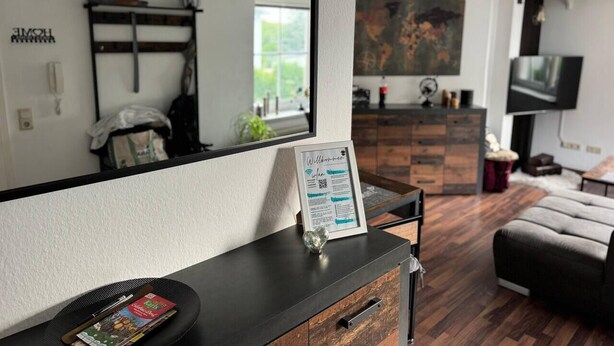 Un salon moderne avec un grand miroir, un panneau d’accueil encadré, un meuble en bois et un canapé.