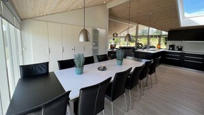 Une cuisine moderne dotée d’un grand îlot central, de chaises noires et d’une table à manger agrémentée de plantes en pot.
