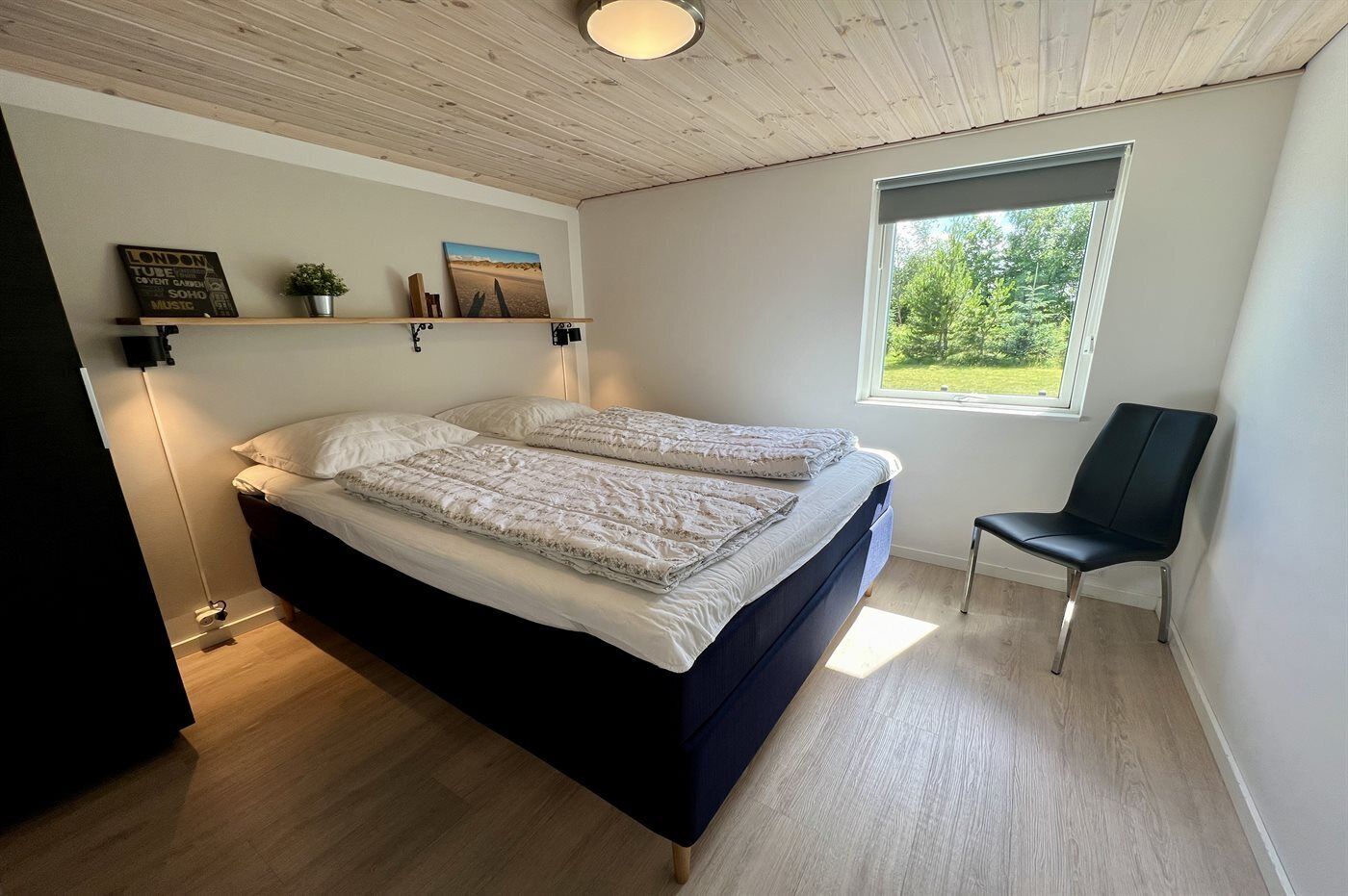 Een slaapkamer met een bed, een stoel, een raam en een plank met spullen.