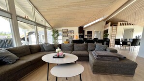 Un salon moderne avec un canapé d’angle, une table basse ronde et un coin repas, la cuisine étant visible au fond.
