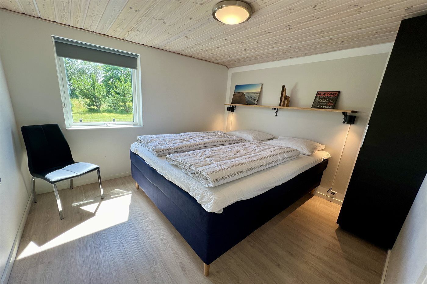 Une chambre à coucher avec un lit, une chaise, une fenêtre et une étagère sur laquelle est posé un panneau.