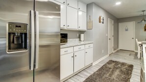Una cocina con un refrigerador de acero inoxidable, cafetera integrada y muebles de cocina blancos.