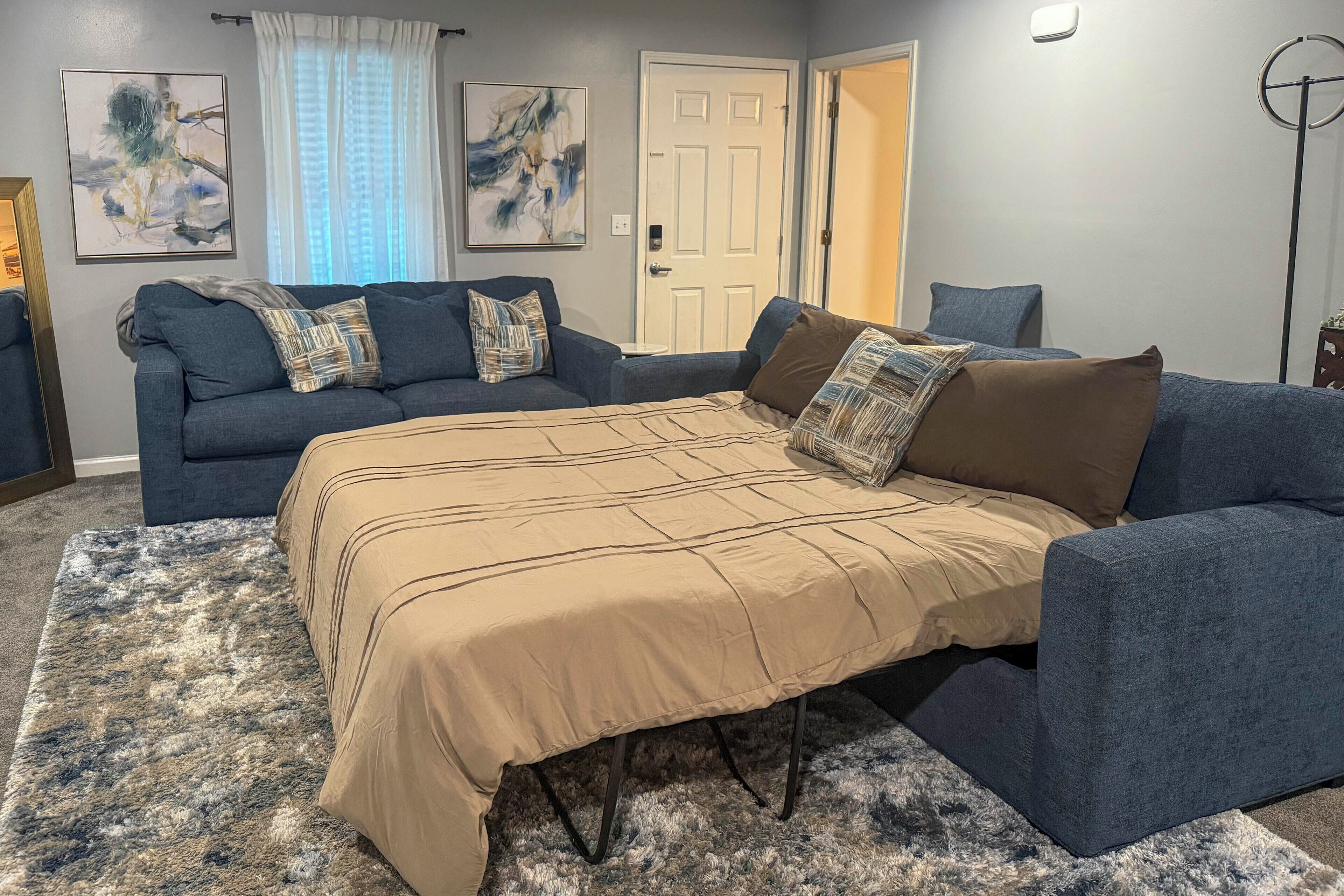 A bedroom with a bed, two sofas, a rug, and artwork on the walls.