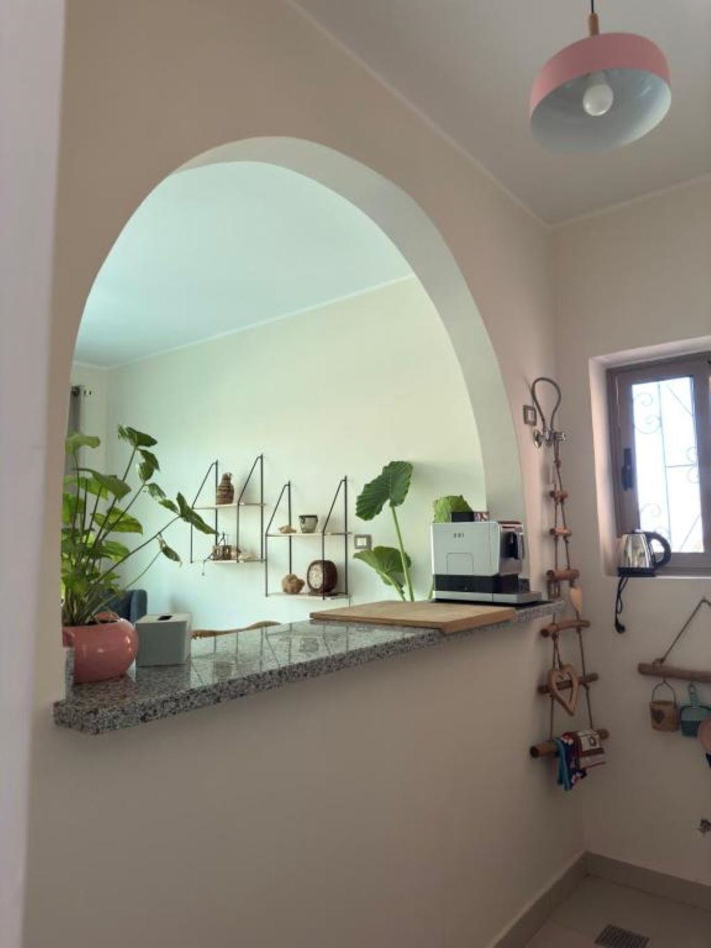 A kitchen with a large archway, a countertop, a microwave, and various kitchen utensils.