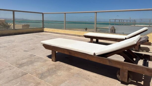 A rooftop terrace with two lounge chairs, a clear view of the sea, and a glass railing. - Villa Anna & Snake - One-Bedroom Apartment with Sea View and Terrace (Red Sea Governorate)