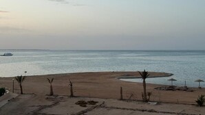 A beach with a sandy shore, a small island, and a boat in the water. - Villa Anna & Snake - One-Bedroom Apartment with Sea View and Terrace (Red Sea Governorate)