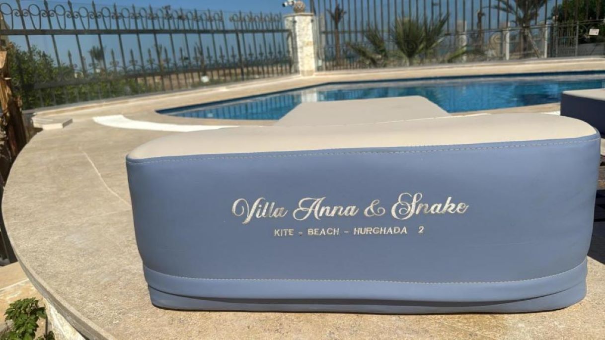 Een ligbed aan het zwembad met de tekst 'Villa Anna & Snake' en 'Kite - Beach - Hurghada 2' erop.