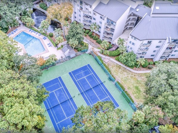Vista aérea de un complejo residencial con cancha de tenis, piscina y abundante vegetación.