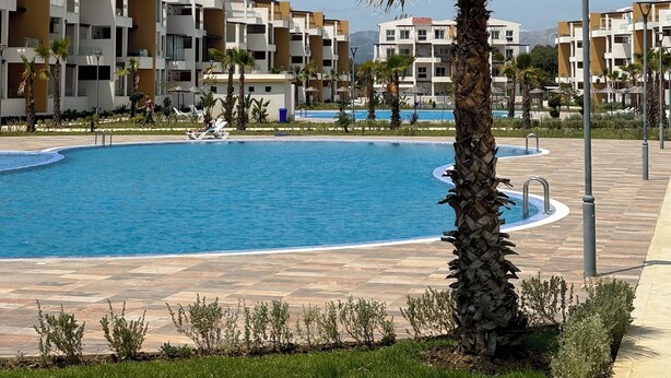 A swimming pool surrounded by modern apartment buildings, with a palm tree and a lamp post in the foreground. - Apartment in a beautiful residence Mirador Golf 3, with 3 large swimming pools (Unknown)