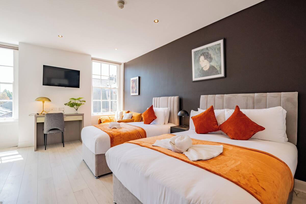 A hotel room with two beds, a desk, a TV, and a window.