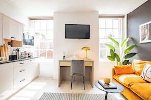 A modern kitchen with a dining area, a desk with a lamp, a sofa, and a TV mounted on the wall. - Dublin Central Suites (Dublin)