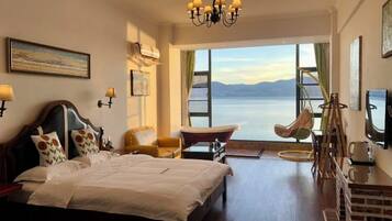 A hotel room with a large bed, a chair, a desk, and a view of the water.
