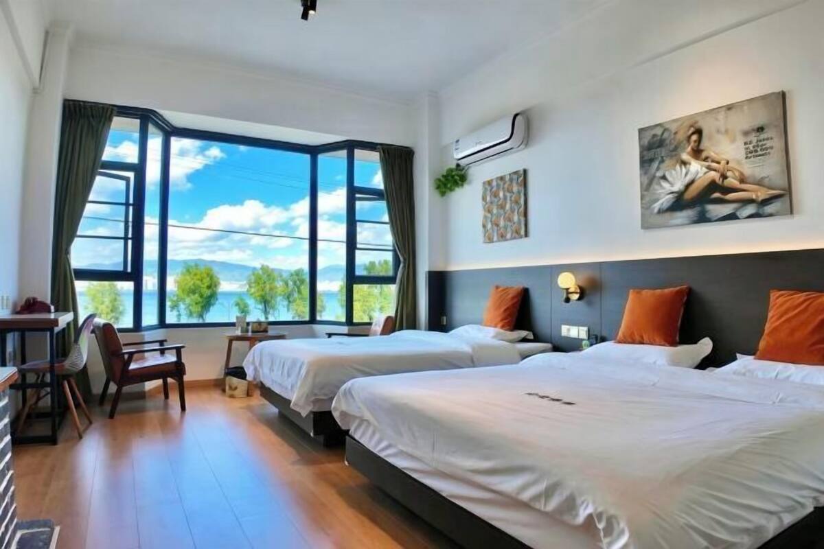 Une chambre d’hôtel avec deux lits, un bureau, une chaise et une grande fenêtre donnant sur l’extérieur.