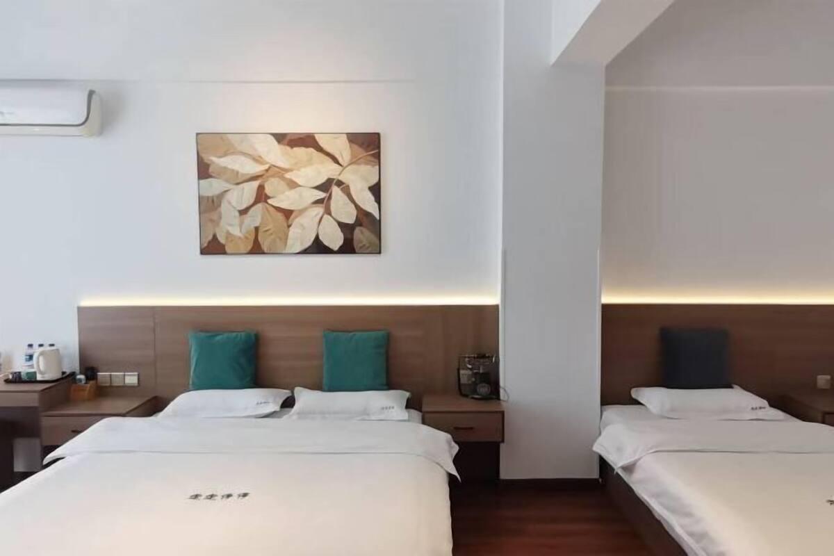 Une chambre d’hôtel avec deux lits, une œuvre d’art accrochée au mur, des tables de chevet et une petite table de nuit avec une radio.