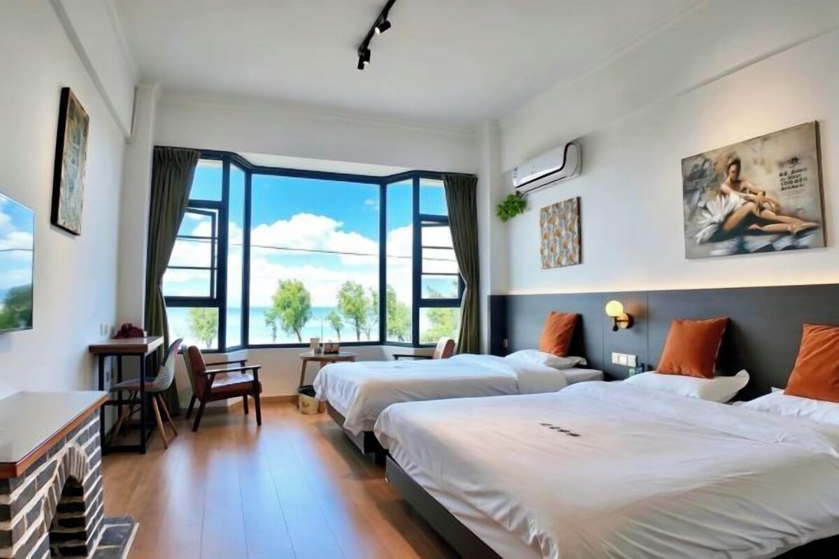 Habitación de hotel con dos camas, un escritorio, una silla, un ventanal con vistas y obras de arte en las paredes.