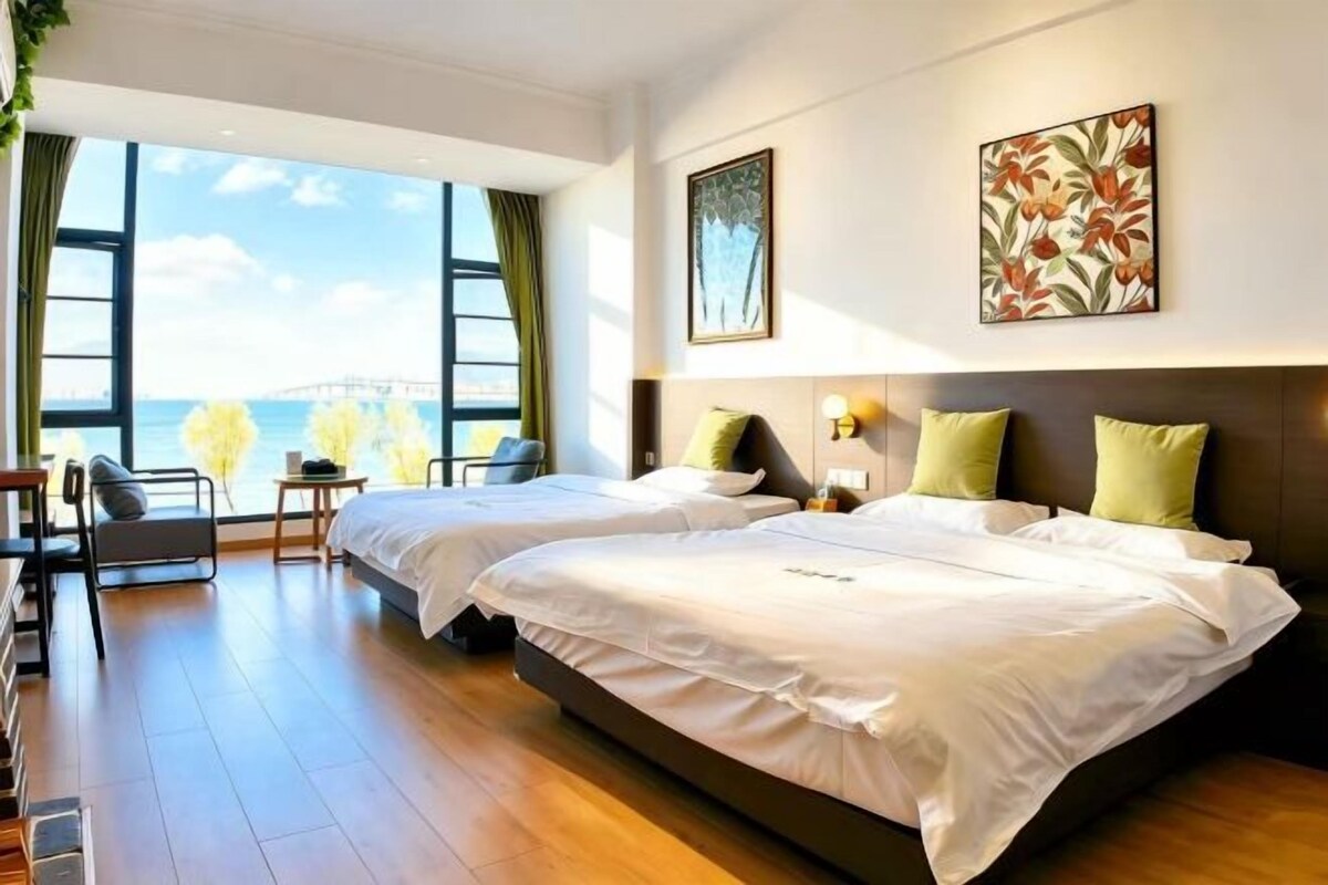 A hotel room with two beds, a desk, and a view of the sea.