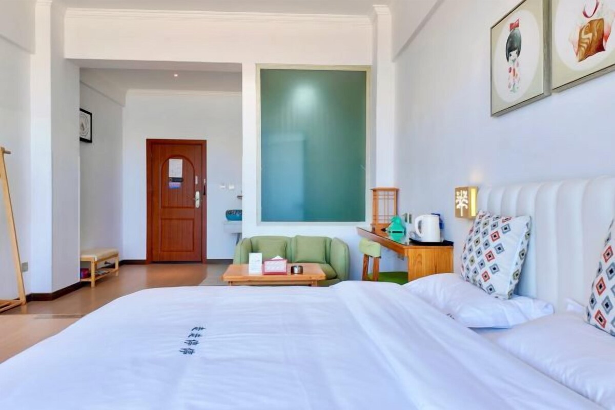 Una habitación de hotel con una cama, un sofá verde, una mesita de madera y un ventanal grande.