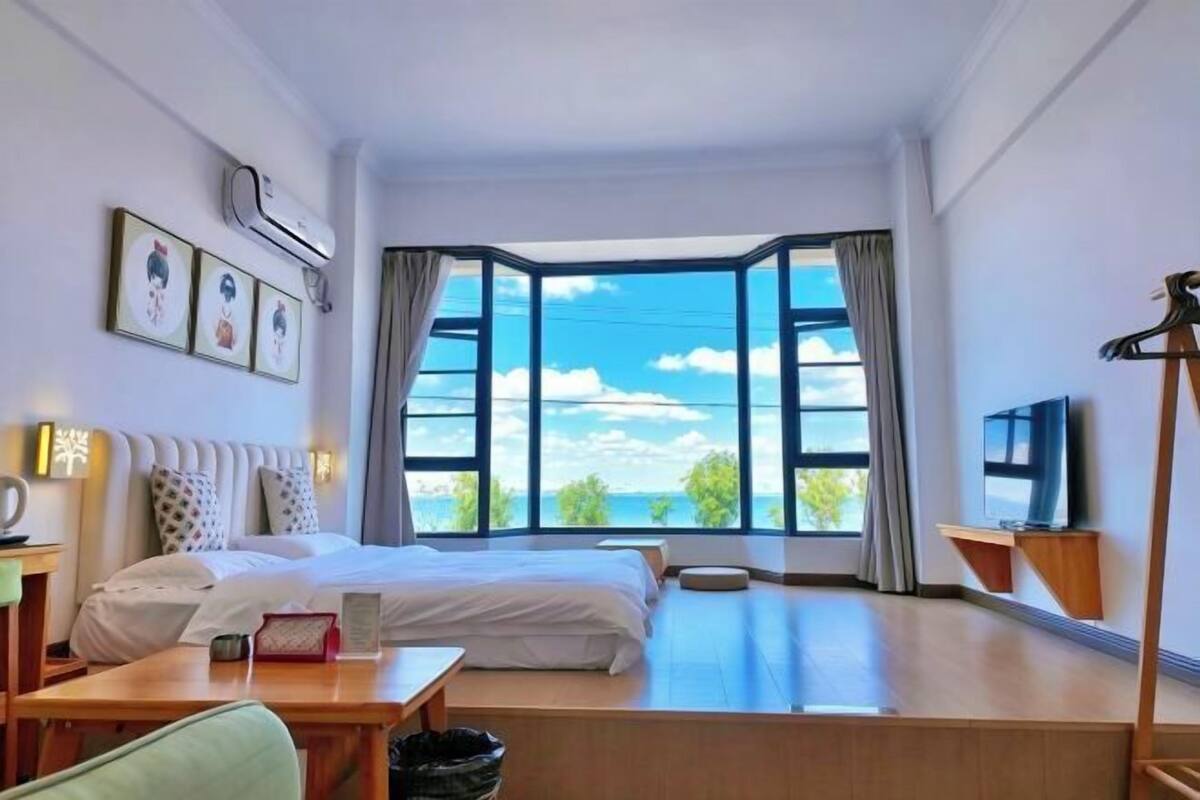 Une chambre d’hôtel équipée d’un lit, d’un bureau, d’une chaise, d’une télévision et d’une grande fenêtre donnant sur un beau paysage.