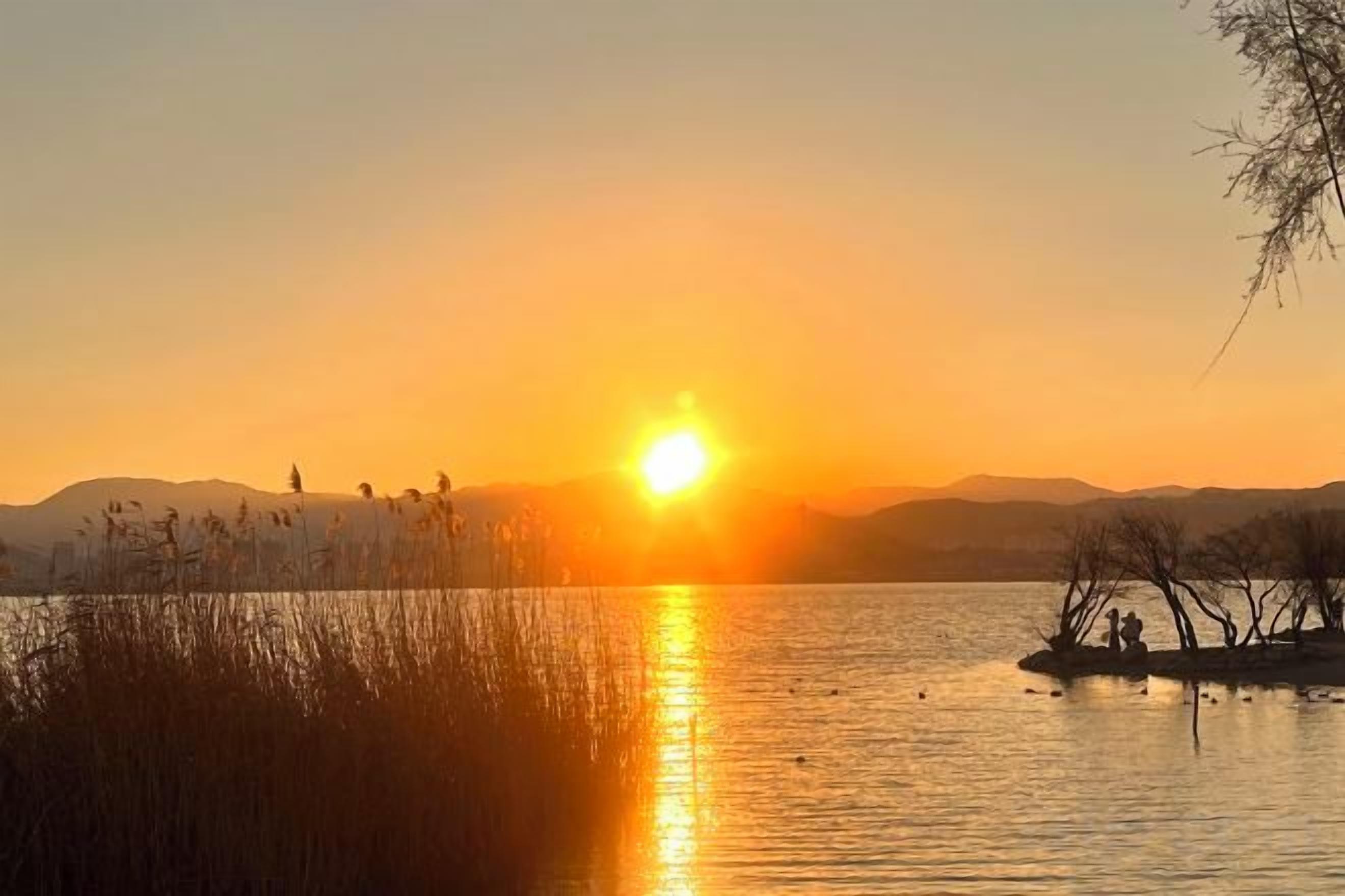 A sunset over a calm lake with distant mountains and a clear sky.