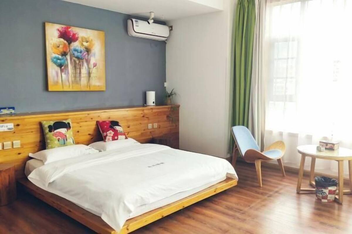 Une chambre d’hôtel avec un lit en bois, un tableau au mur, un appareil de climatisation et une vue sur l’extérieur.