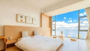 Quarto de hotel com uma cama grande, uma mesa de cabeceira, uma pequena mesa e vista para o mar.