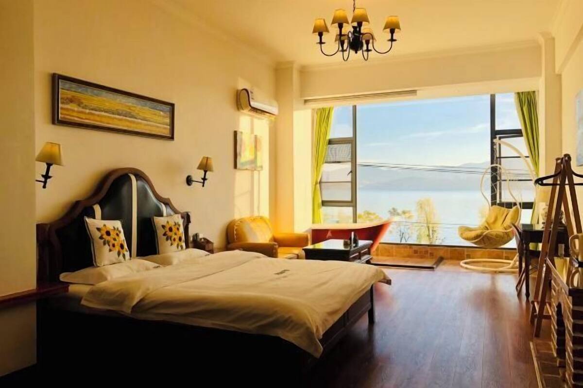 Une chambre d’hôtel avec un lit, un bureau, une chaise, une vue sur la mer et un lustre.