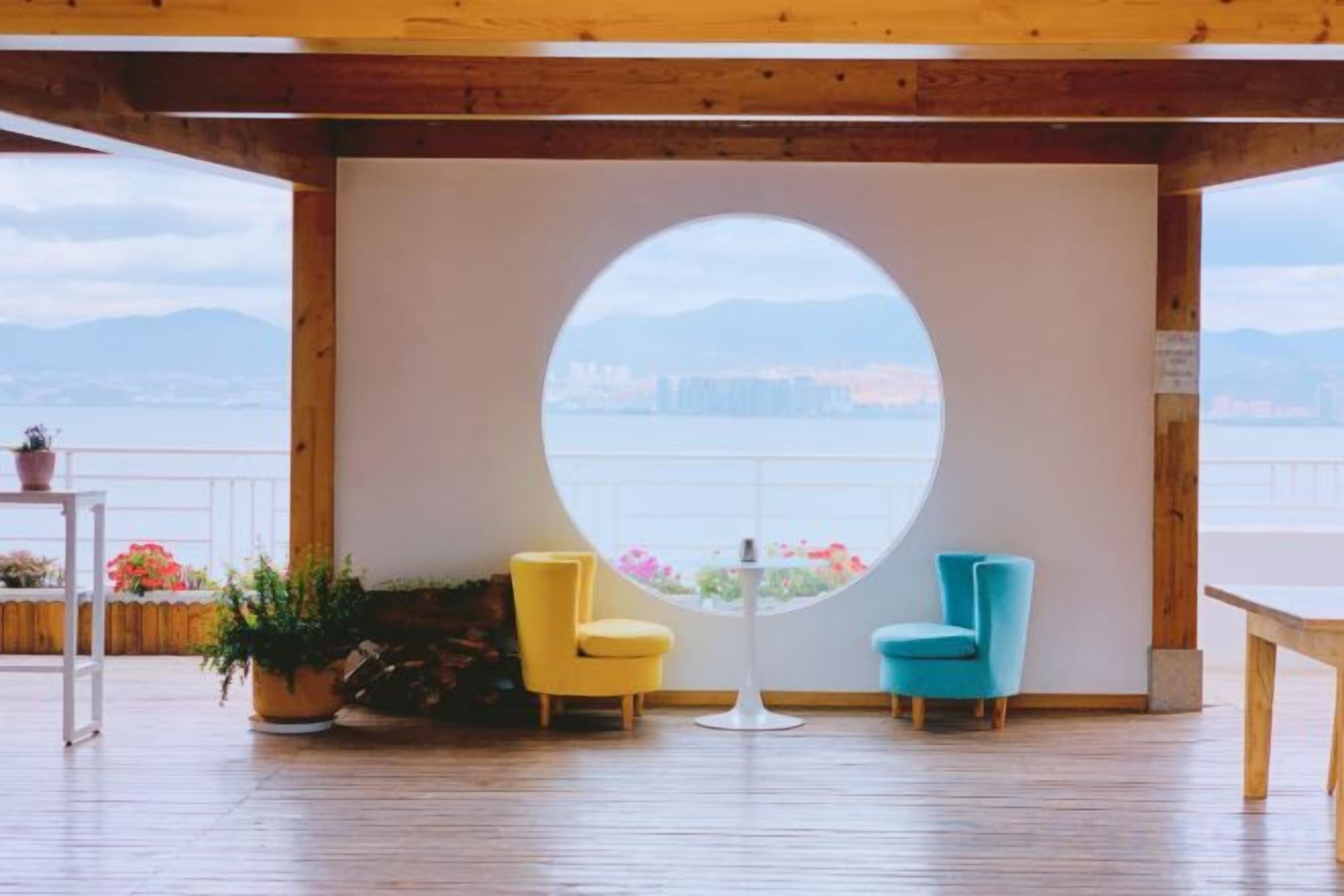 A room with a circular window, two chairs, a table, and a view of a cityscape.