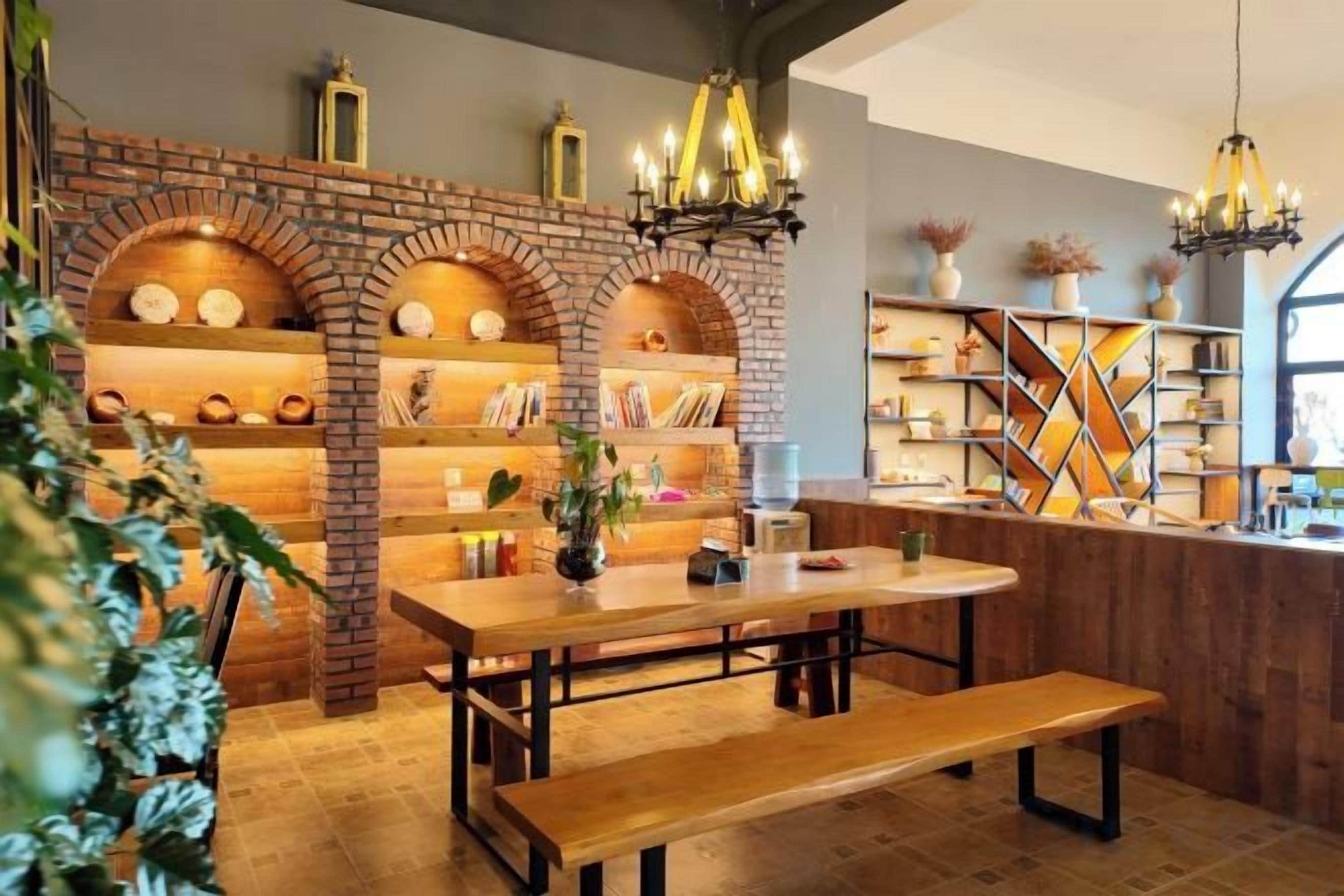 A cozy dining area with a wooden table and bench, brick shelving with decorative items, and a chandelier.